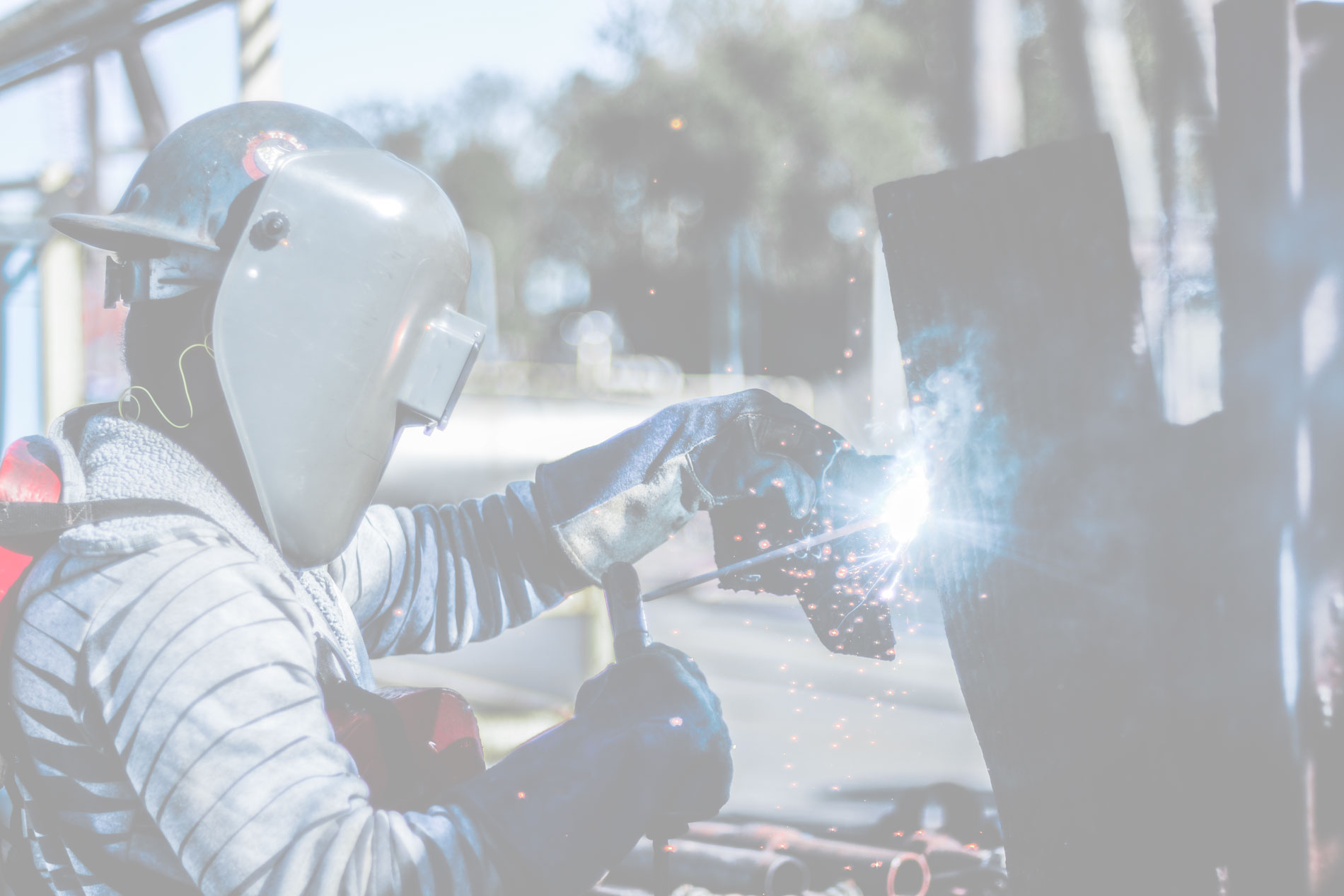 Welder in a protective helmet striking an arc on a steel fabrication job