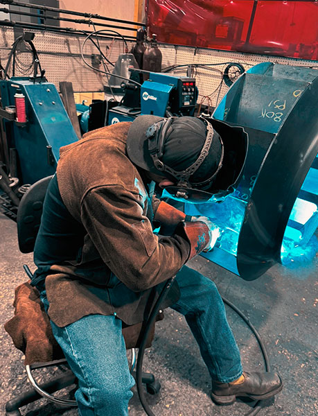 Welder kneeling to repair production equipment on site