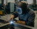 Certified welder in protective gear welding steel structure, hiring certified welder